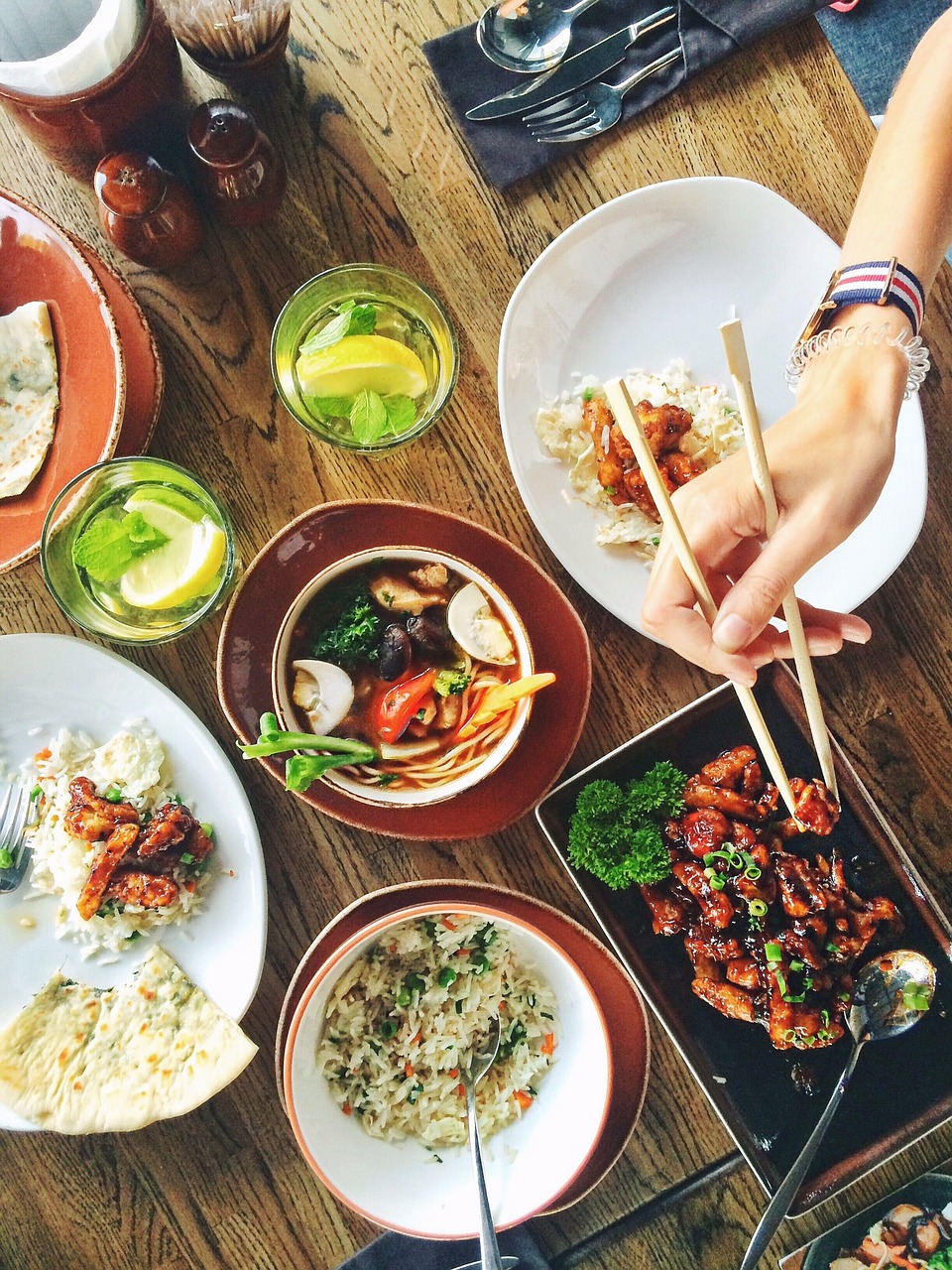 Photo of table with food and hand holding chopsticks.
