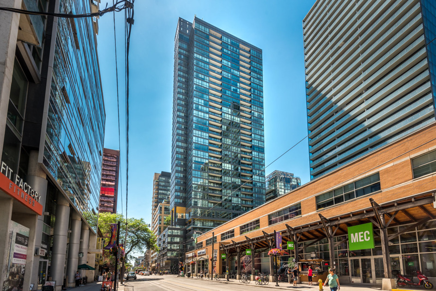 Daytime view of Charlie Condos from street surrounded by shops and condos.