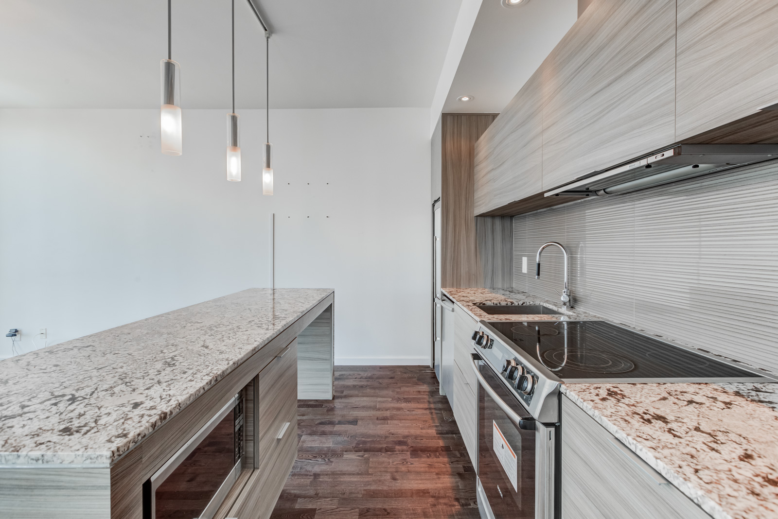 Heavily-textured kitchen with marble counters, laminate floors, stainless steel appliances, wooden cabinets and hanging lights.
