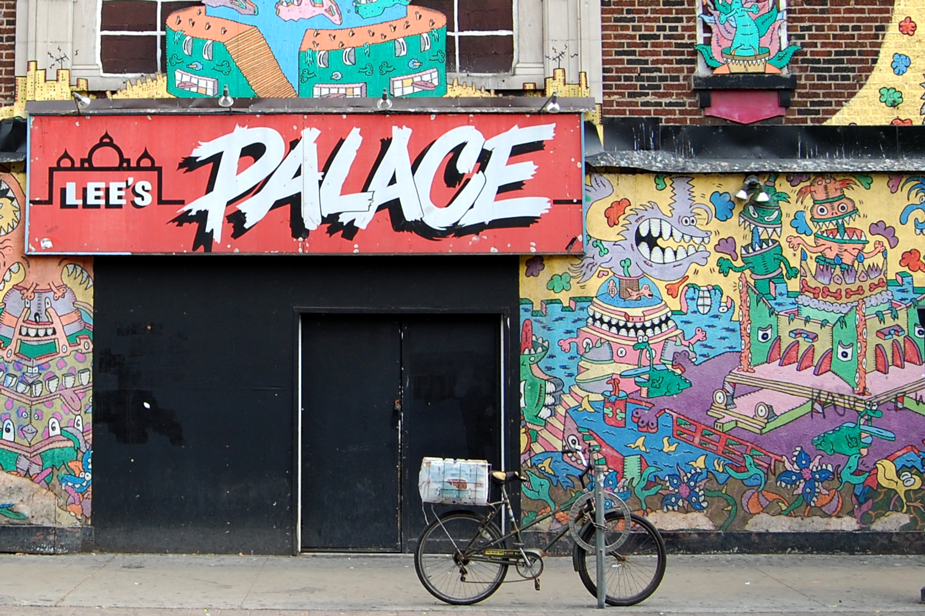 Red and white sign for Lee's Place in The Annex; colourful graffiti on walls and bicycle chained to parking meter.