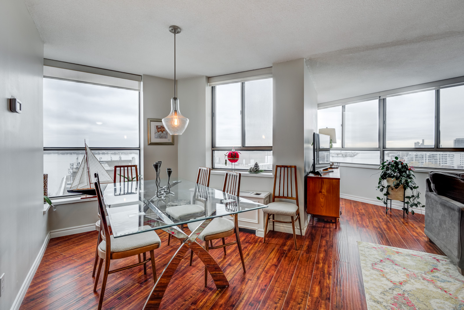 Dining room with clear glass table, red floors and window with view of Toronto Waterfront.
