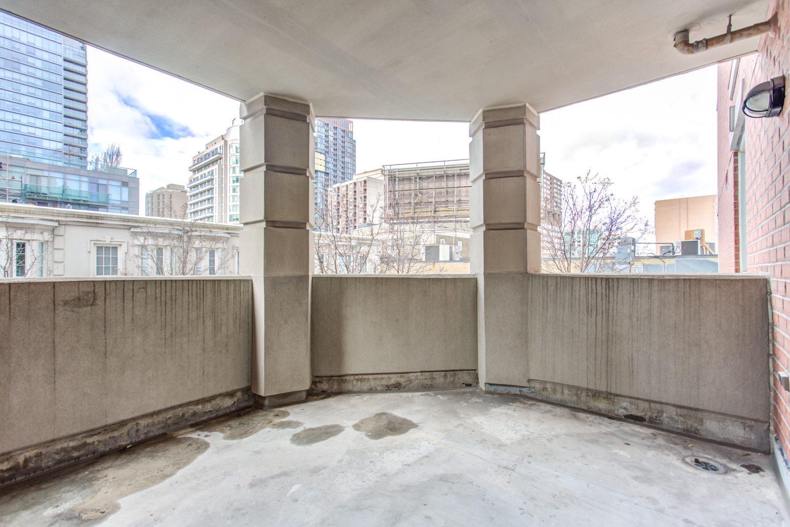 Concrete balcony of 20 Collier St Unit 408 with columns and view of Yorkville beyond.