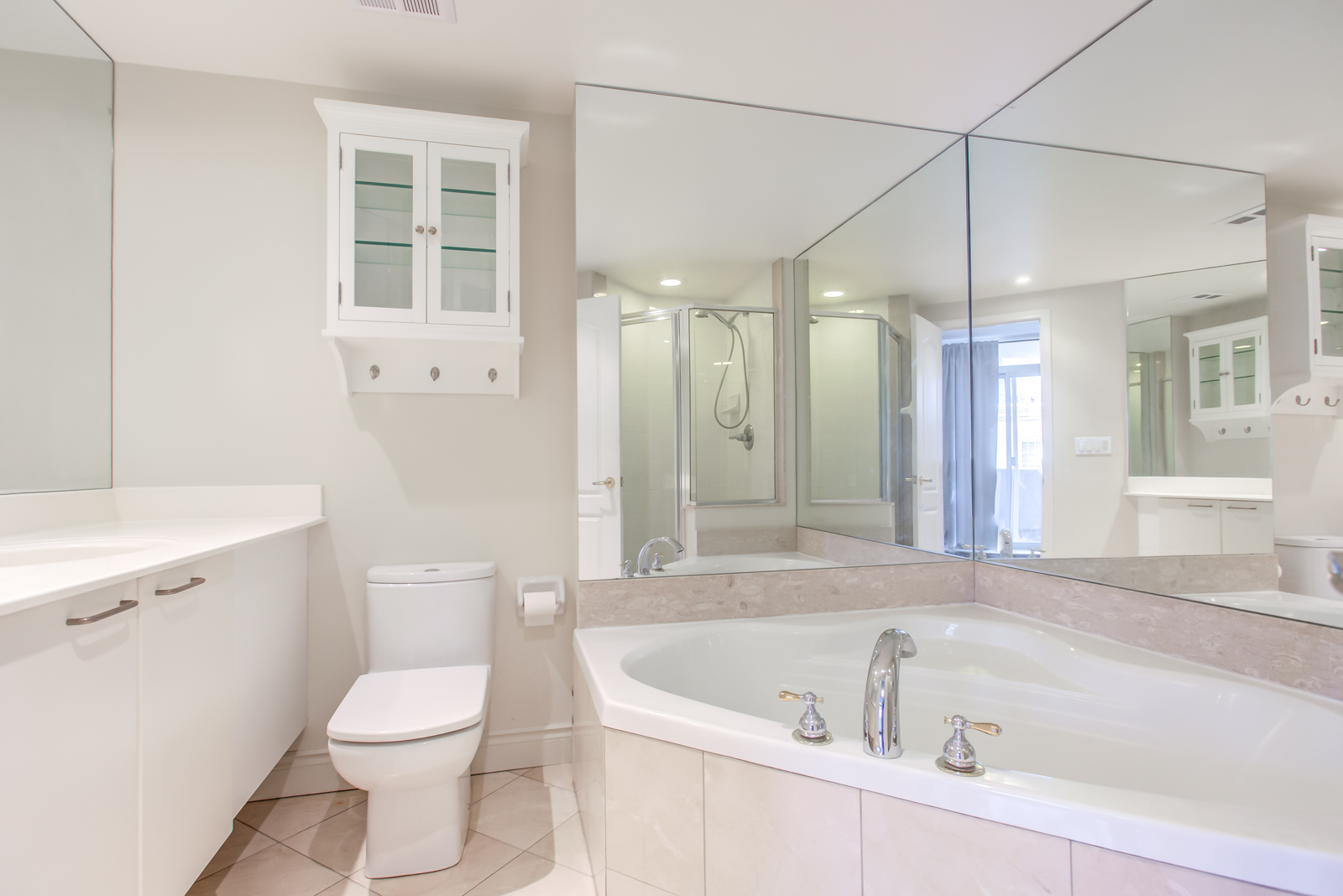 Ensuite bath with Jacuzzi, white sink and cabinet, and wall-to-wall mirrors.
