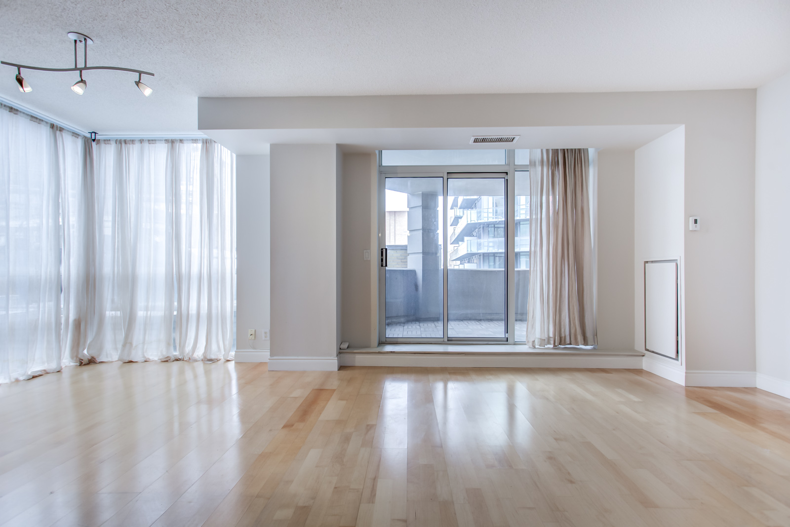 Spacious and empty living room of 20 Collier St Unit 408 showing balcony and white curtains.