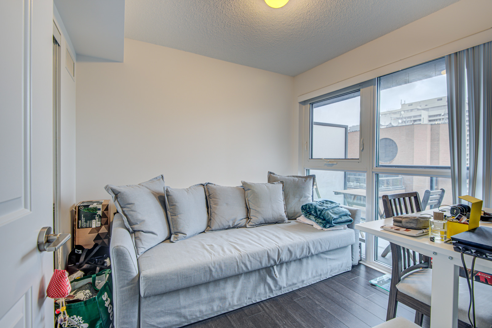 Den with gray couch, table and grocery bags in corner.