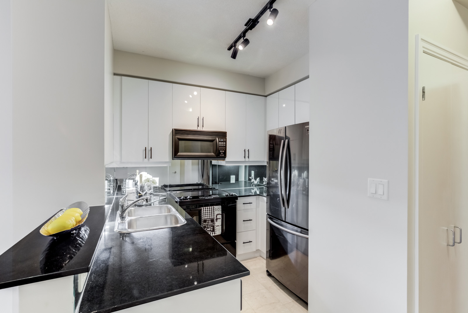 Shiny black granite counters, sleek white cabinets, black appliances and track-lights.