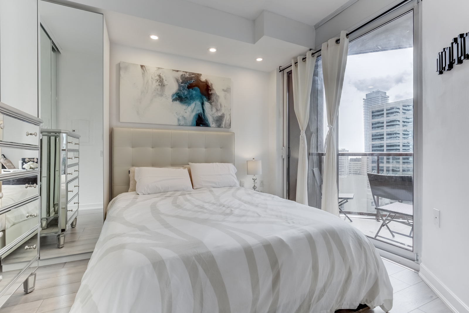 Fully-furnished master bedroom with white queen-sized bed and white laminate floors.