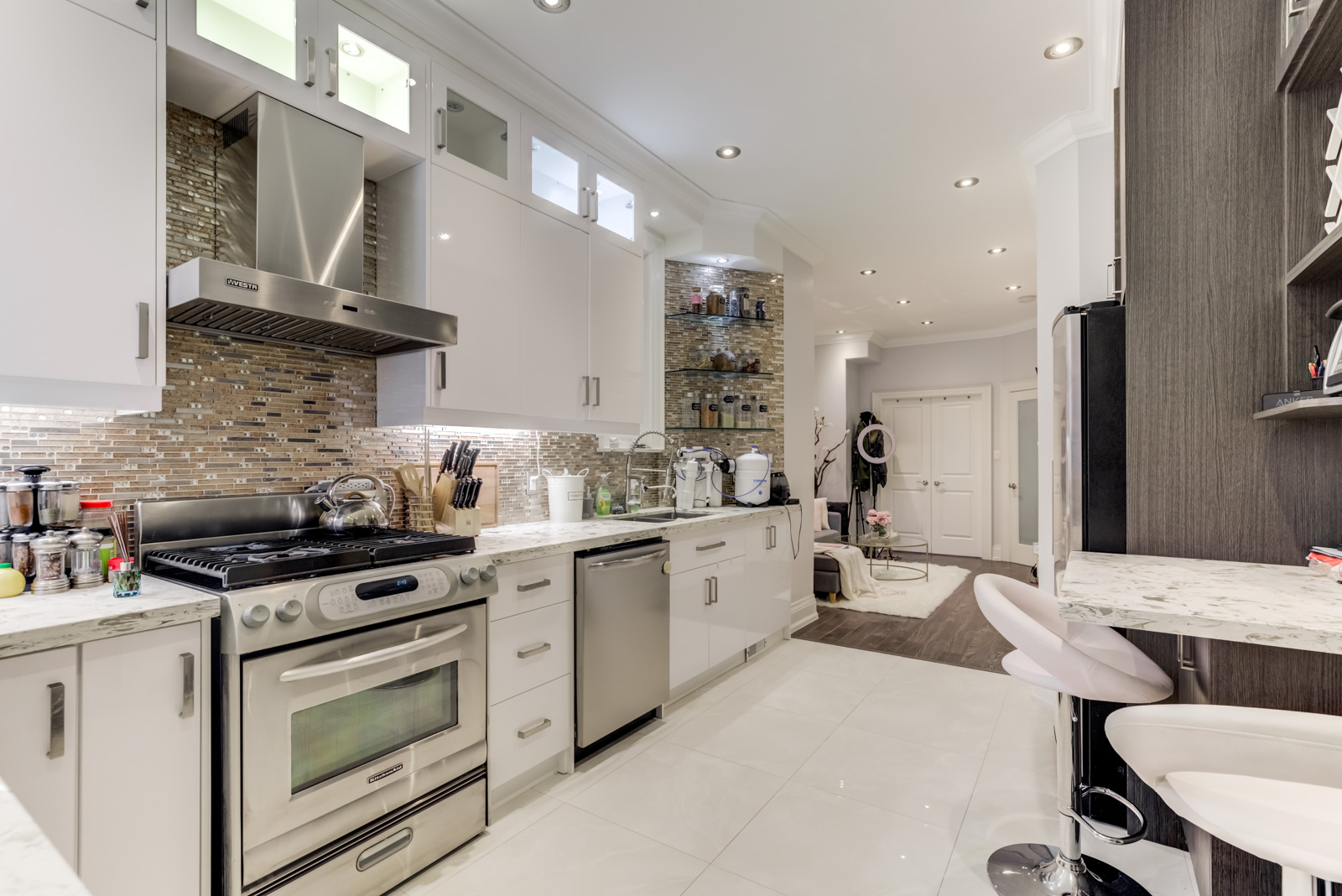 Gorgeous renovated kitchen with modern appliances, shiny white cabinets and tiled backsplash.