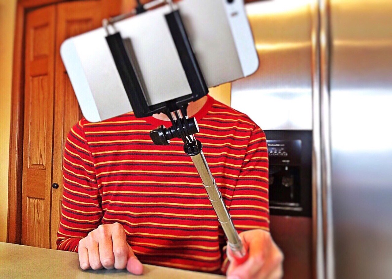 Man in house holding selfie stick with phone.