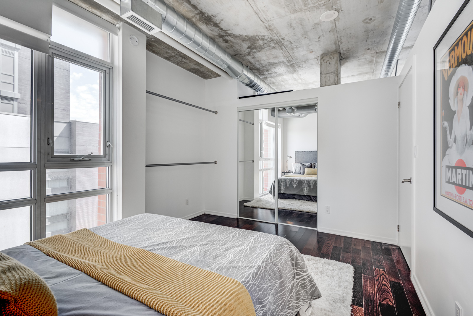 Soft loft master bedroom with exposed ductwork, concrete ceiling and low gray walls.