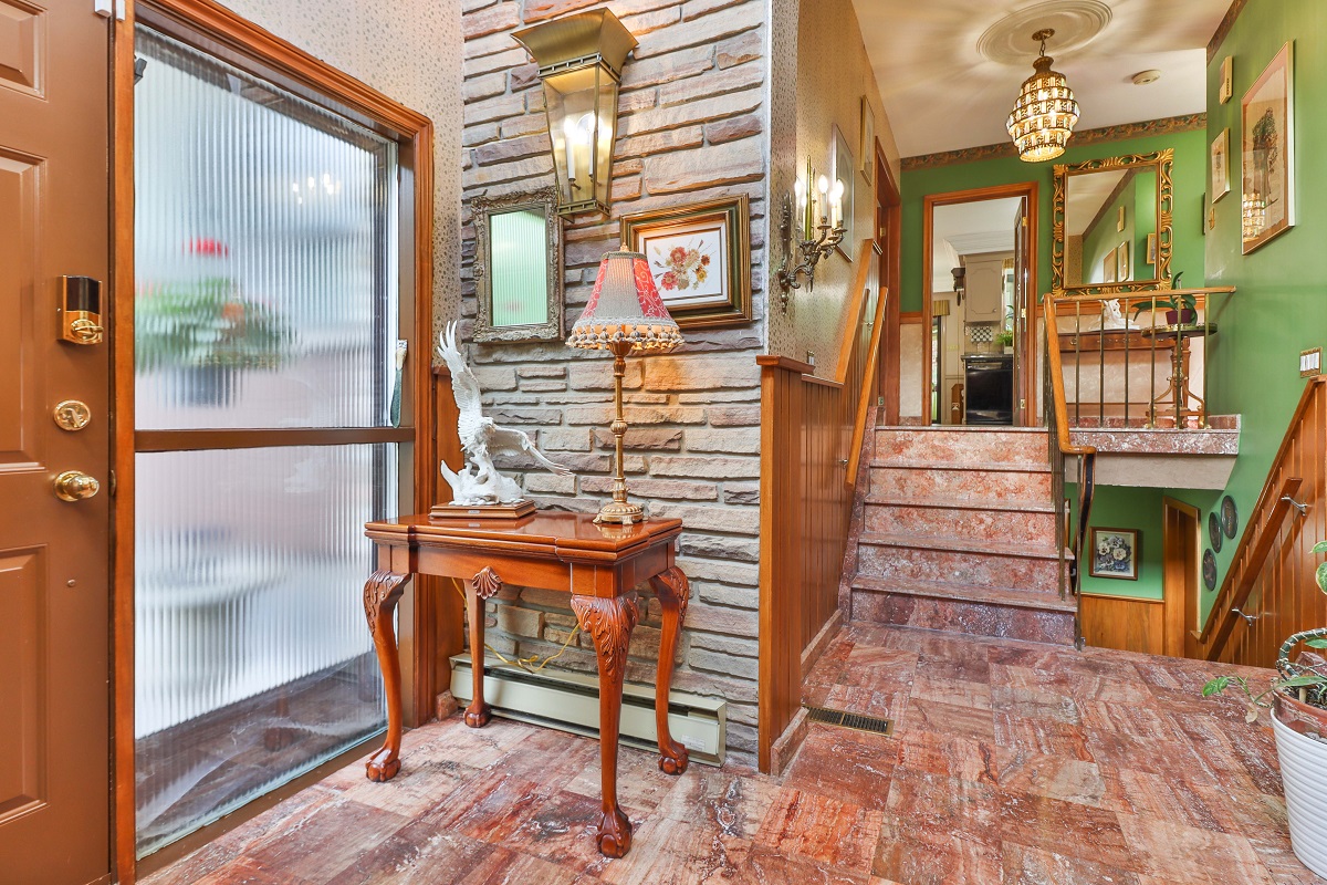 Opulent front entrance with reddish marble floors, wood panels, brick walls and antique furniture.