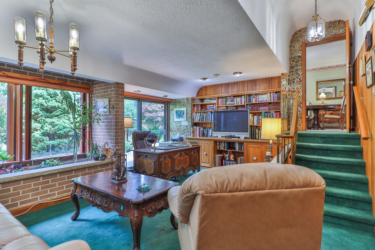 Bungalow library with wood paneling, chandeliers and green broadloom carpet.