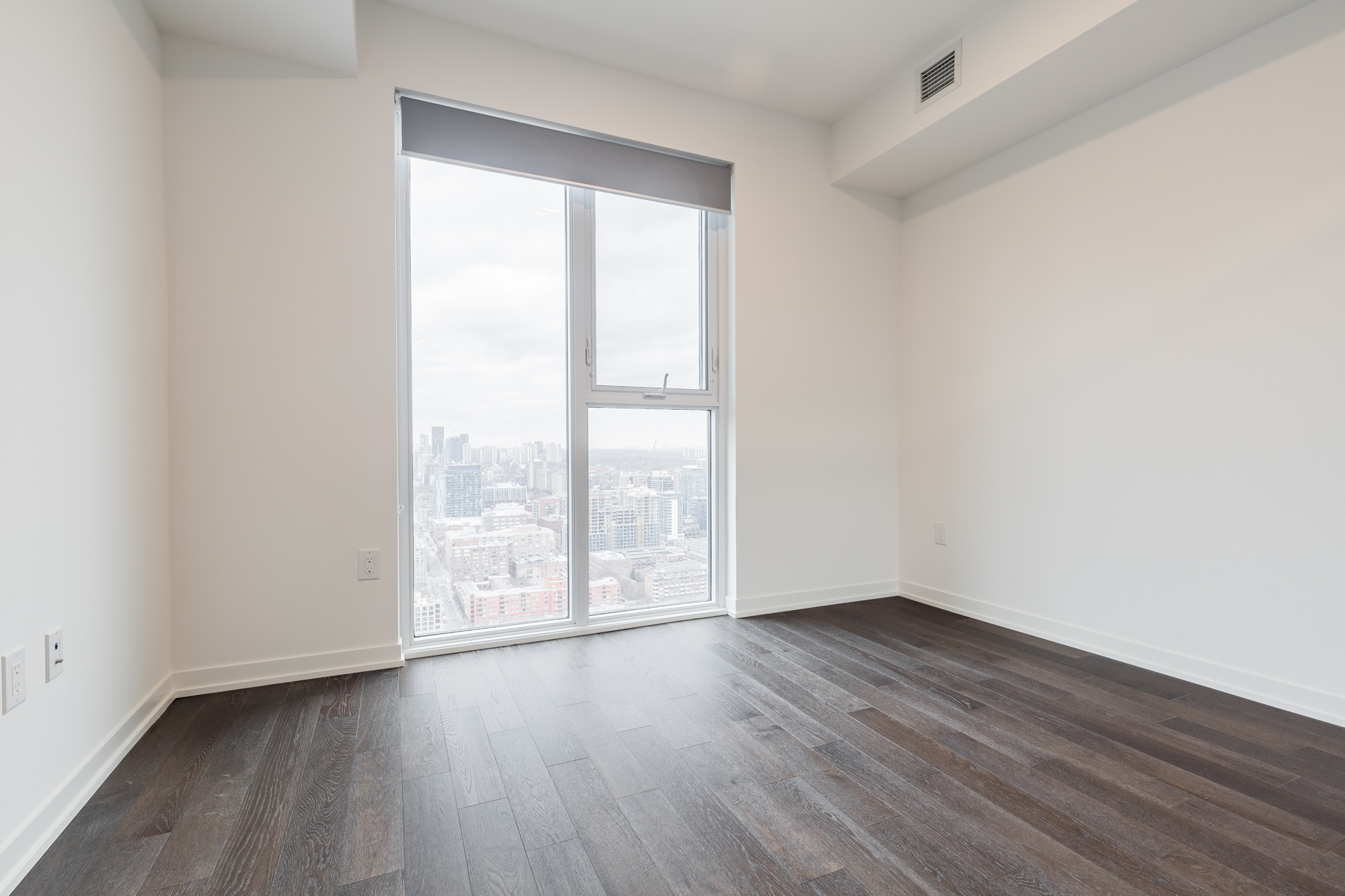 Photo of empty condo bedroom with hardwood floors and big window.