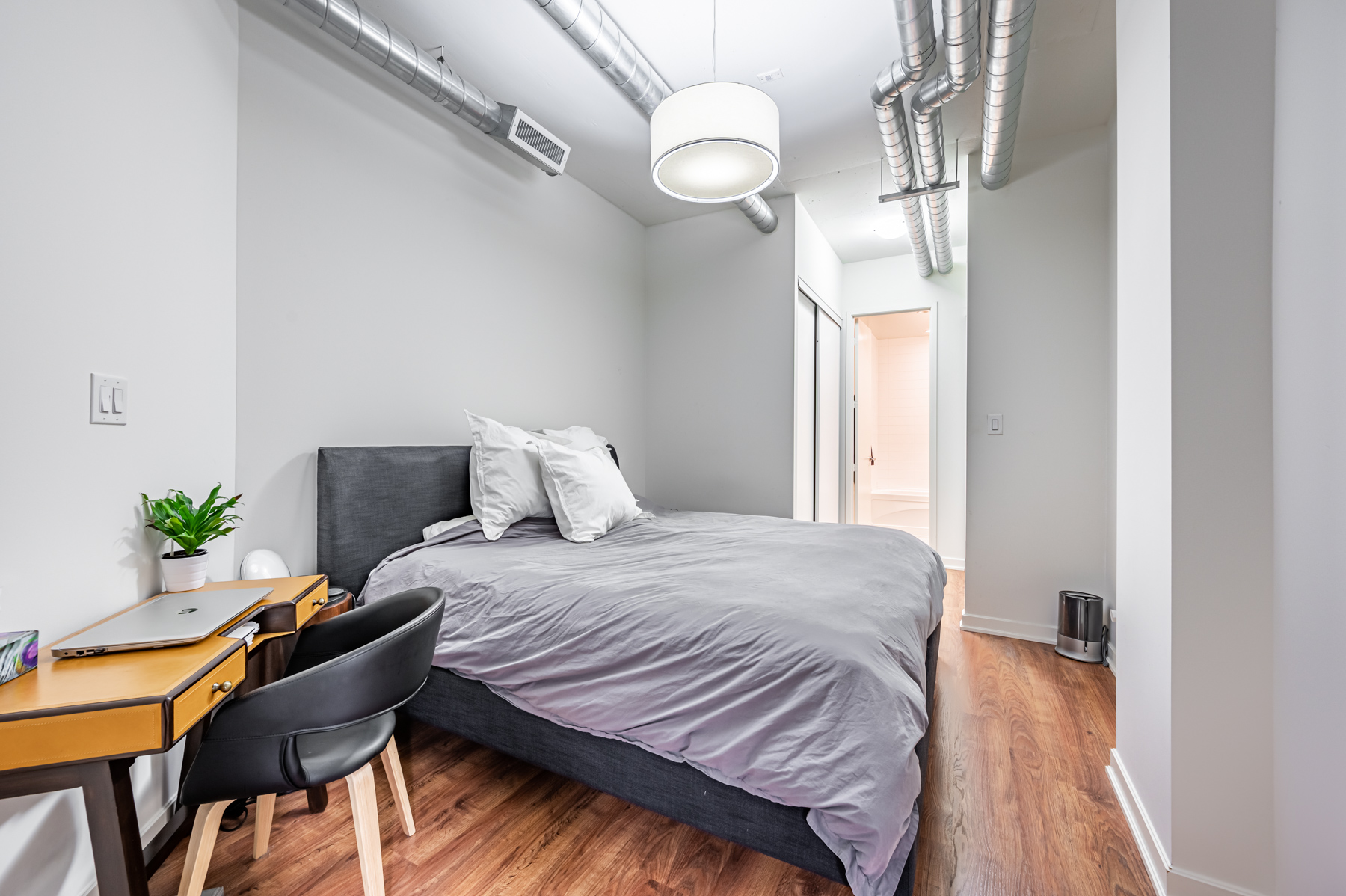 master bedroom industrial design hardwood floors modern light fixture 380 Macpherson Ave Unit 517 master bedroom with exposed pipes, modern lighting and hardwood floors.