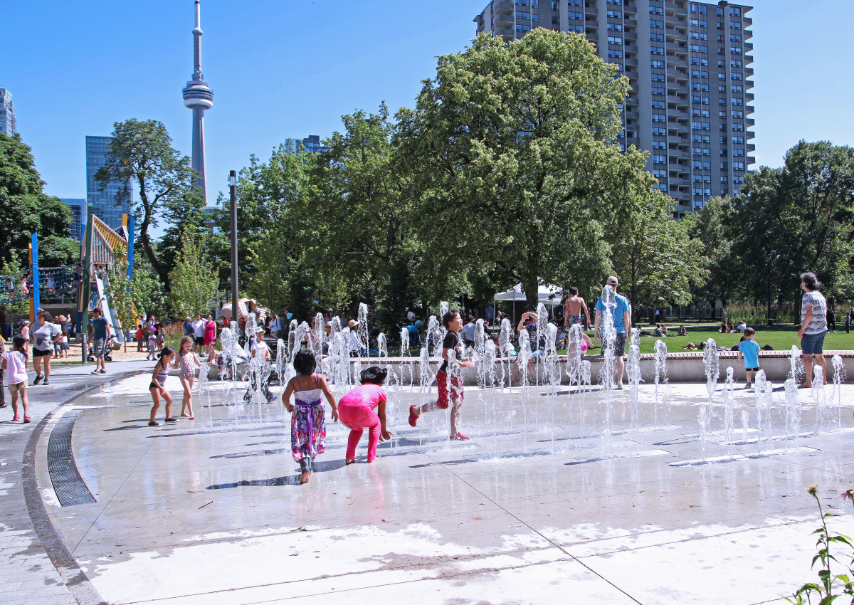 Grange Park splash-pad with kids playing and CN Tower in background.