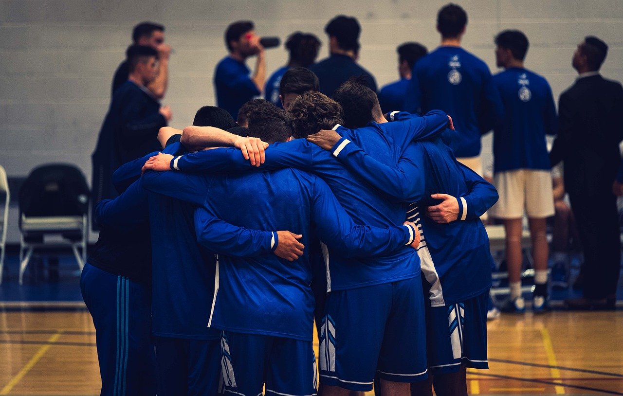 Boys basketball team in blue jerseys in team huddle.
