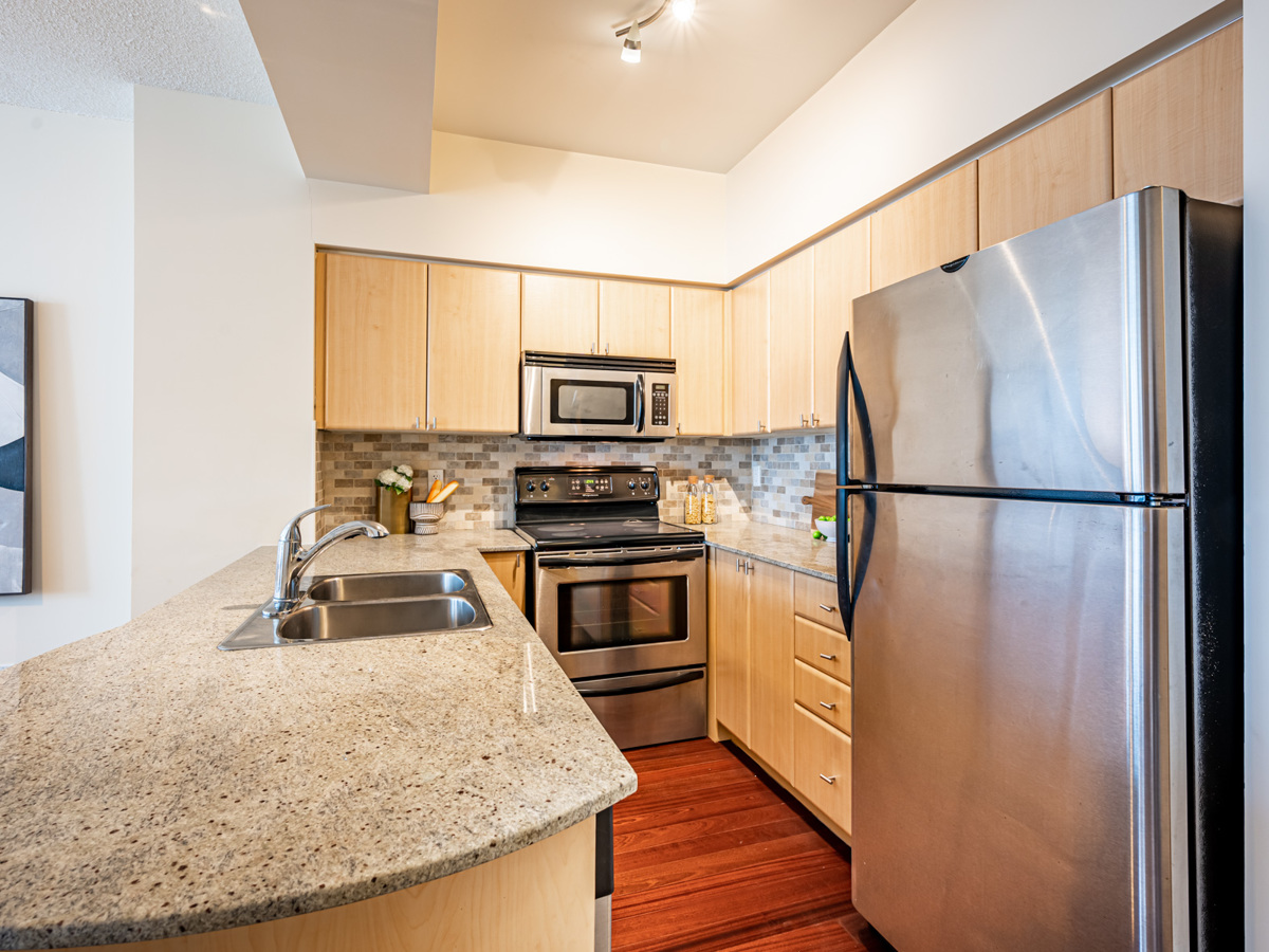 u shaped kitchen beige cabients and drawers silver appliances U-shaped condo kitchen with beige cabinets and drawers.