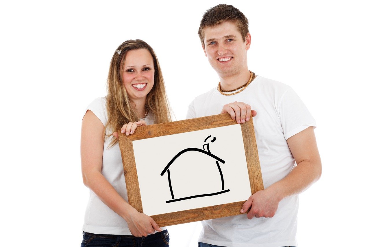 Young couple holding picture frame with house.