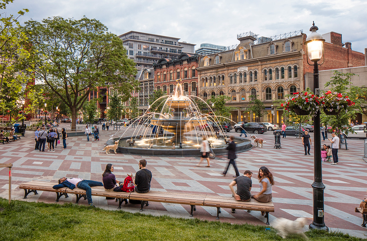 People relaxing and talking at Berczy Park with giant dog fountain at centre.