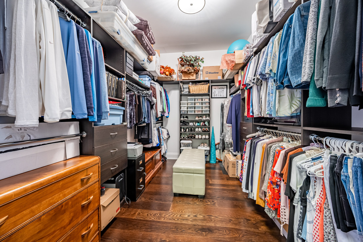 Huge walk-in closet with clothes, shoes, bench, shelves and drawers.