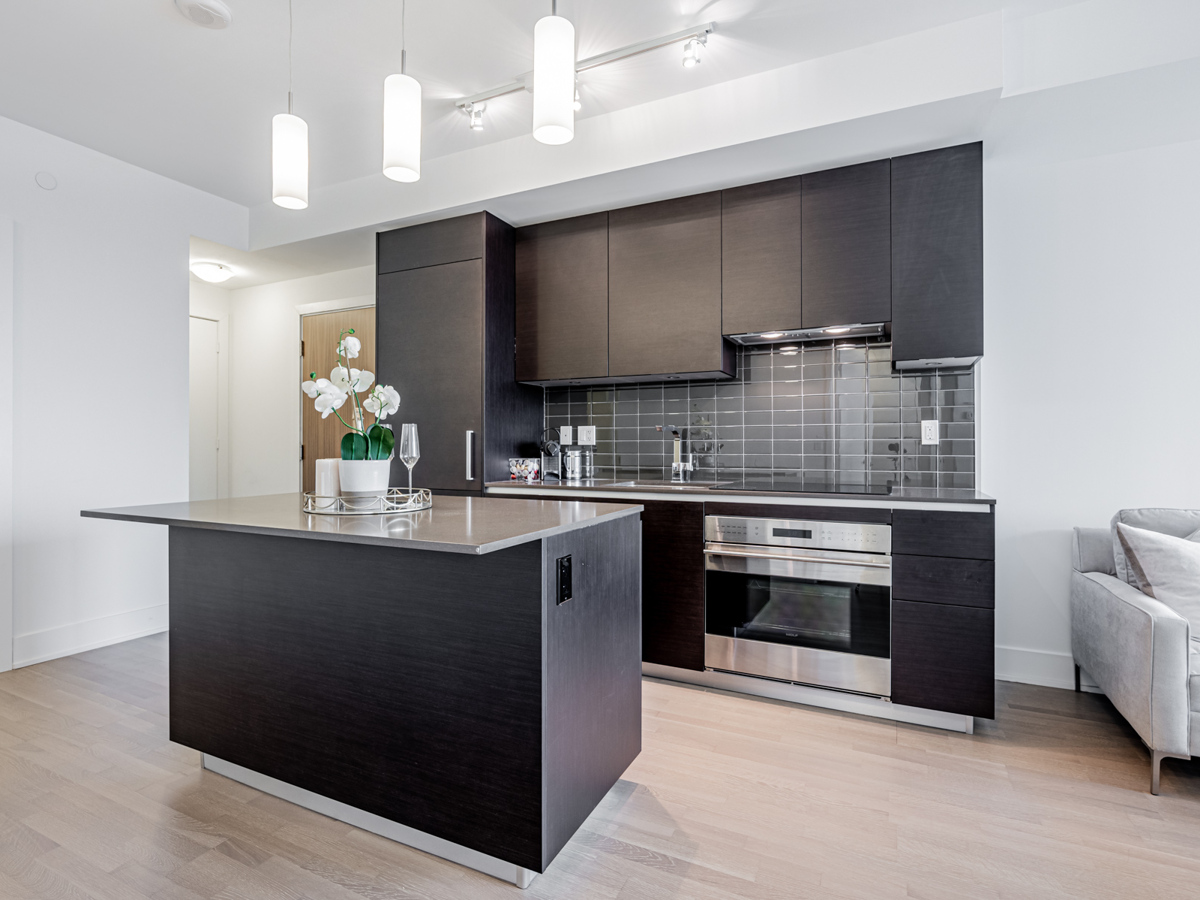 200 Bloor St W Unit 2405 kitchen with dark cabinets, shiny backslash and cylindrical lamps.