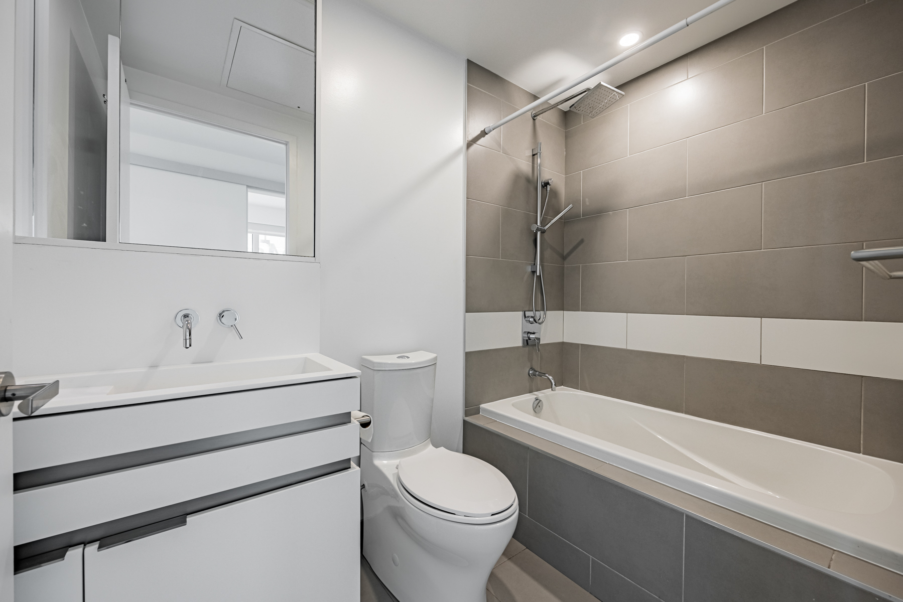 197 Yonge St Unit 2209 primary bath with porcelain tiles, Corian sink, dual showerheads and soaker tub.