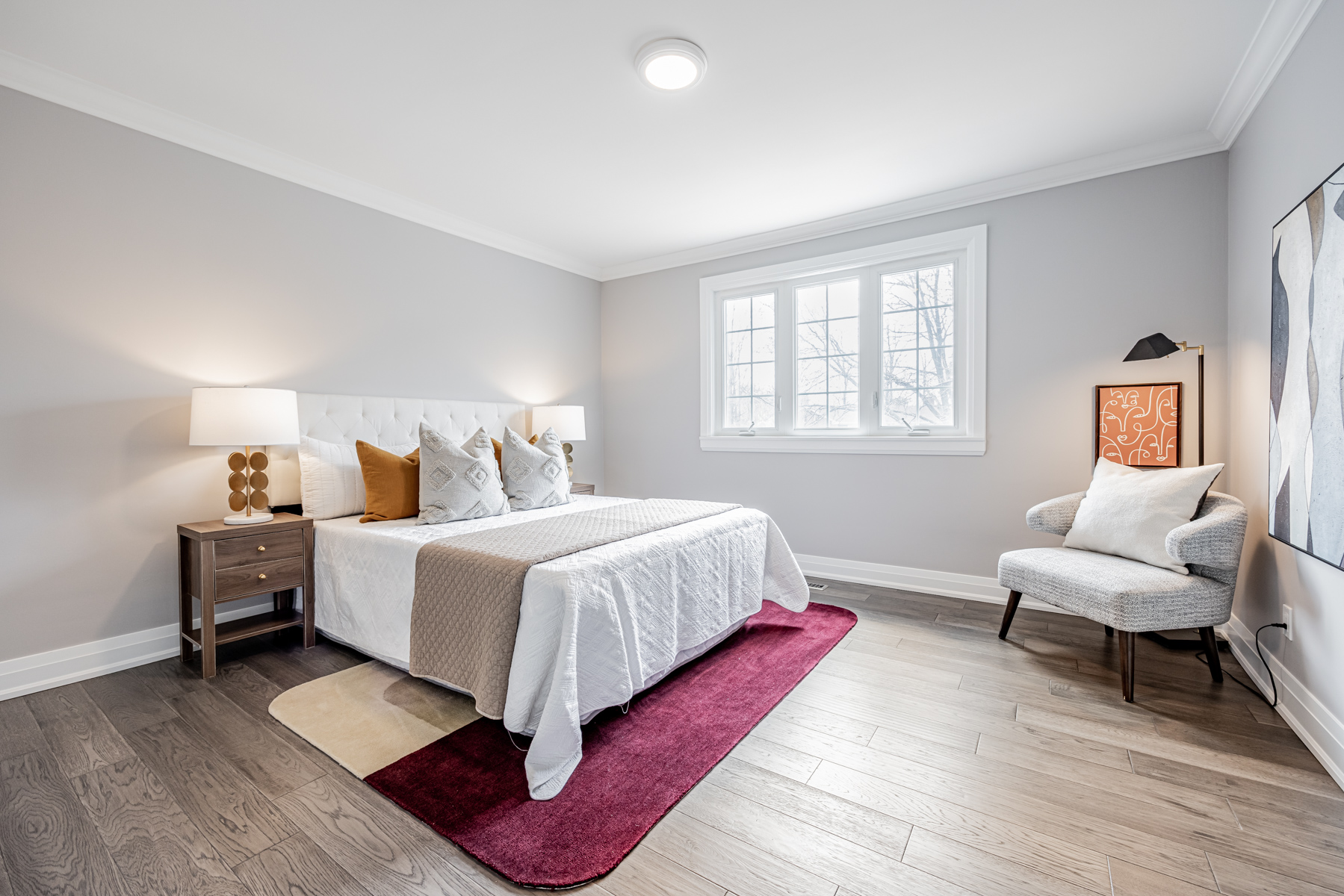 Large bedroom with hardwood floors, gray walls & casement windows.