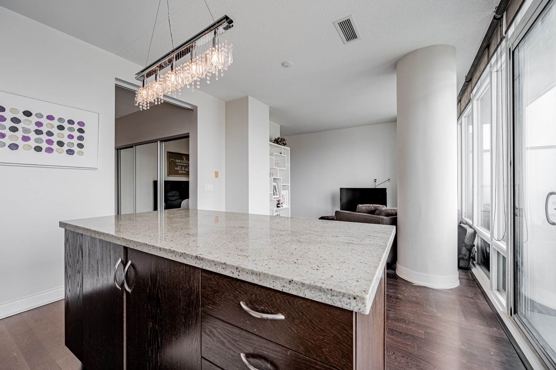 Condo kitchen with classy chandelier hung over centre island.