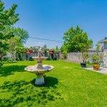 Backyard with fountain, trees, shrubs, garden plots and high fence.