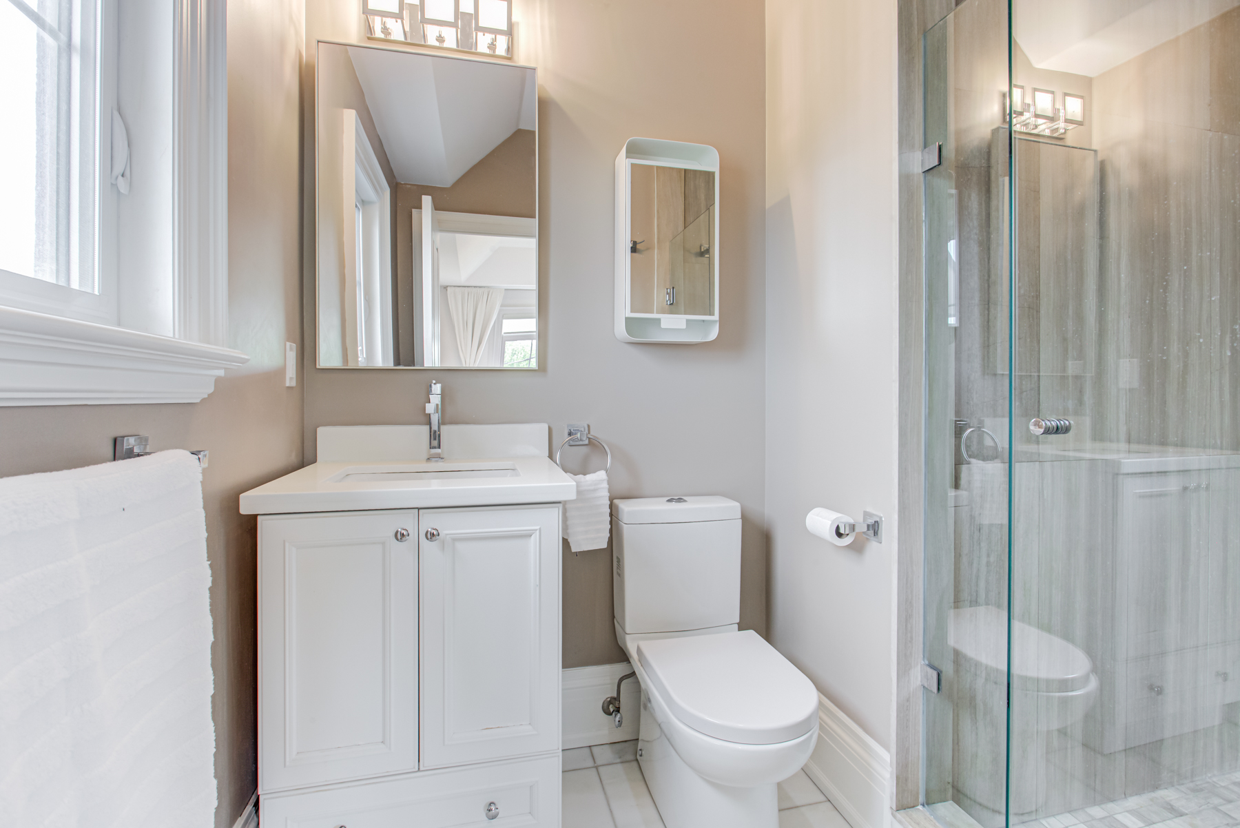Ensuite bath with white vanity, medicine cabinet and frame-less glass shower.