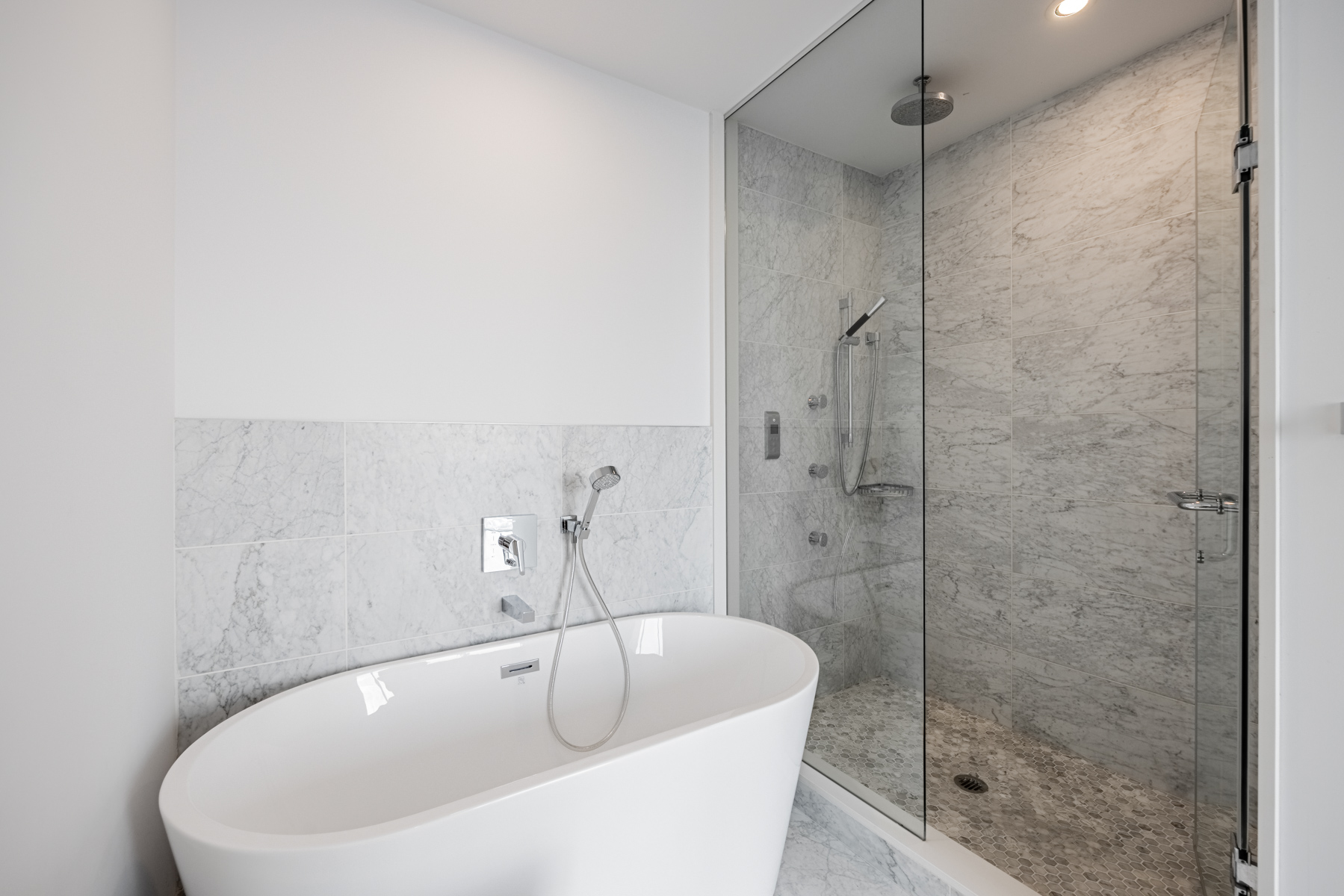 Condo bathroom with freestanding soaker tub and frameless glass shower with stone tiles.