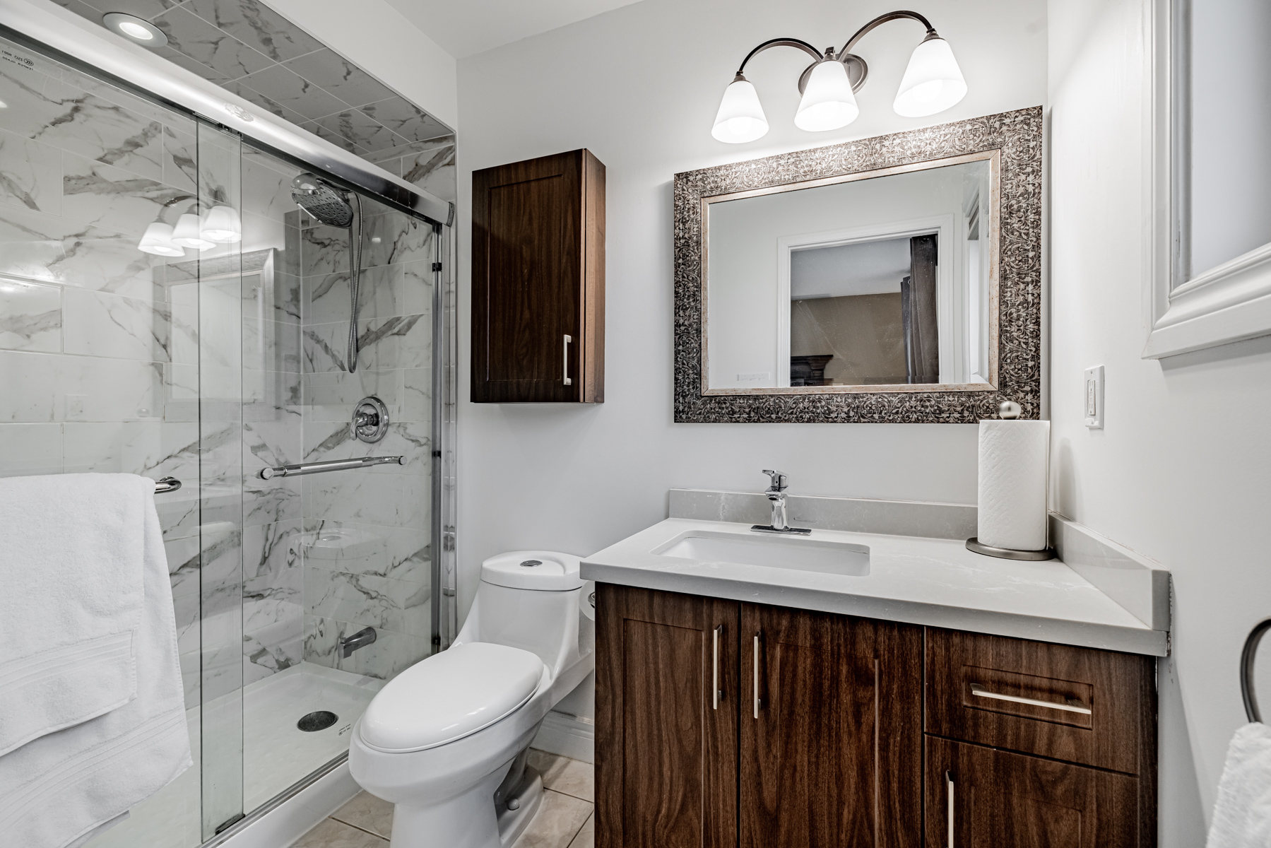 14. 77 Schouten Cres Ensuite bath dark wood cabinets ceramic floors mirror walk in shower 77 Schouten Cres bathroom with gray walls, dark wood cabinets, mirror and walk-in shower with gray-white tiles.